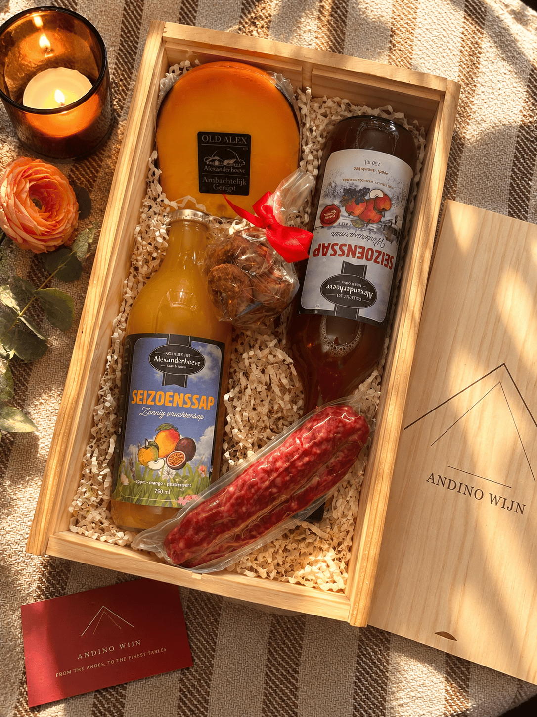 An alcohol-free Andino Wijn corporate gift box holding a bottle of Seizoenssap Zonnig Vruchtensap, a bottle of Seizoenssap Winterwarmer, a wedge of aged Gouda, sliced Metworst and bon bons