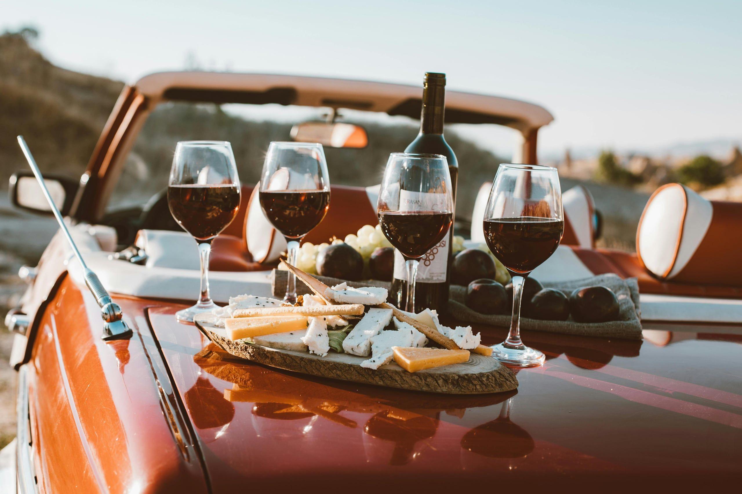 Red wine glasses and a cheese board on the boot of a vintage convertible at sunset