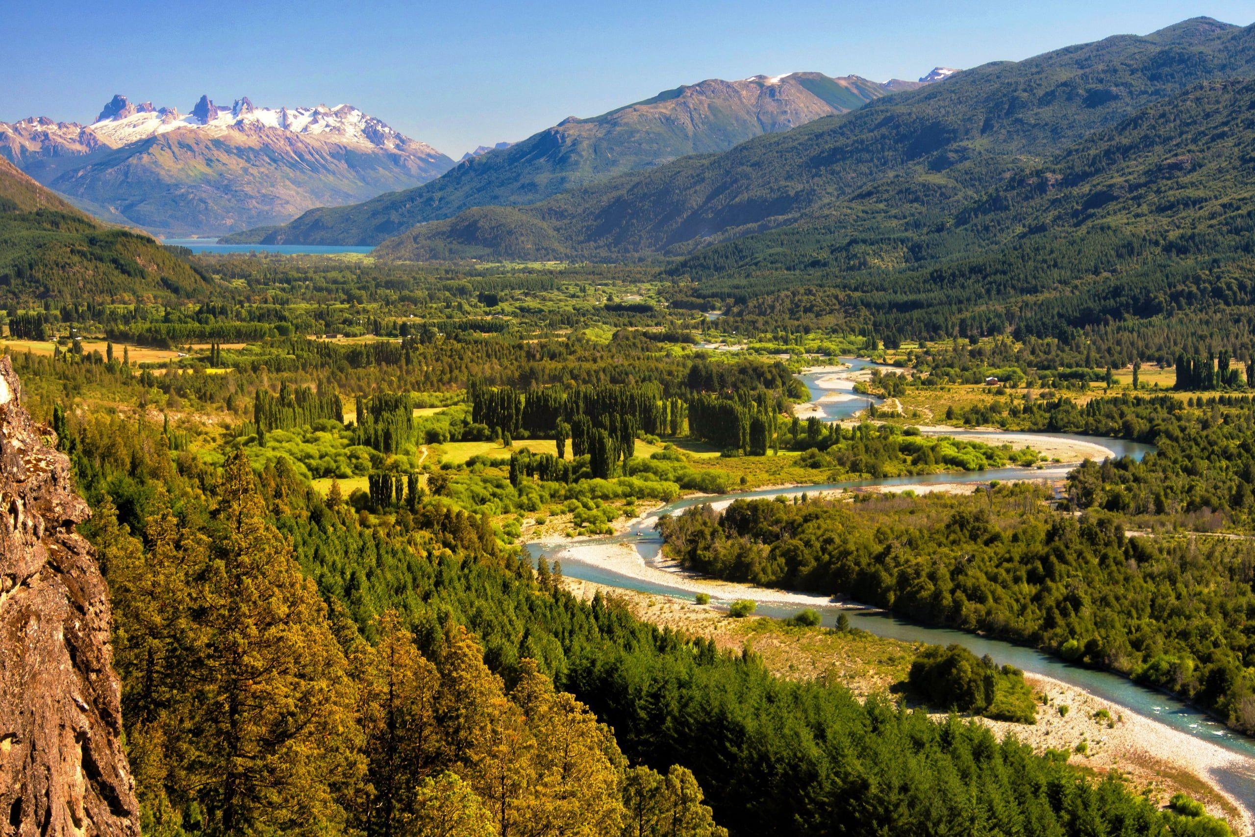 A river winding through a broad green valley beneath forested mountains in Patagonia