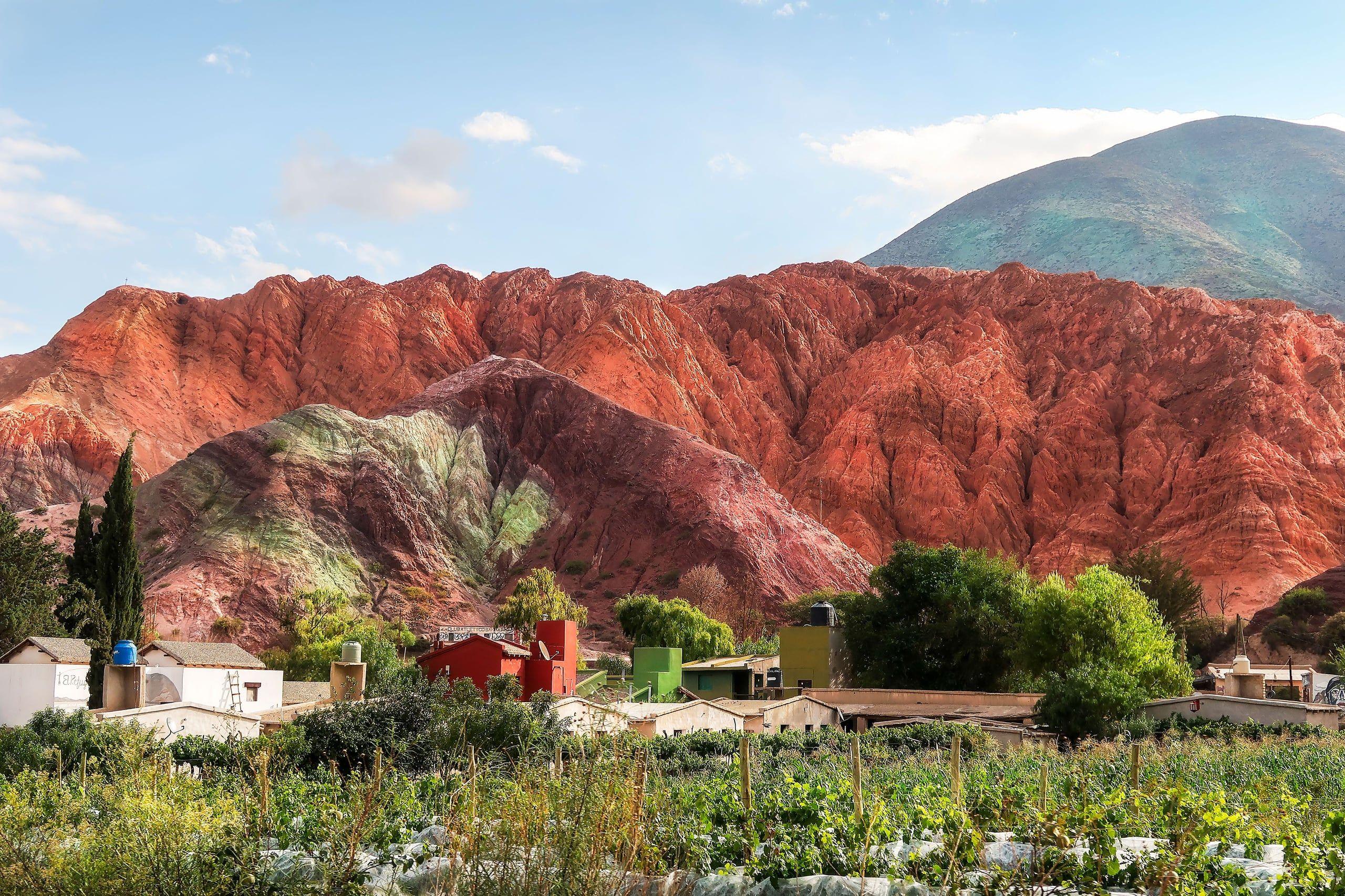 Vivid red rock mountains above cultivated green fields and a village in Salta